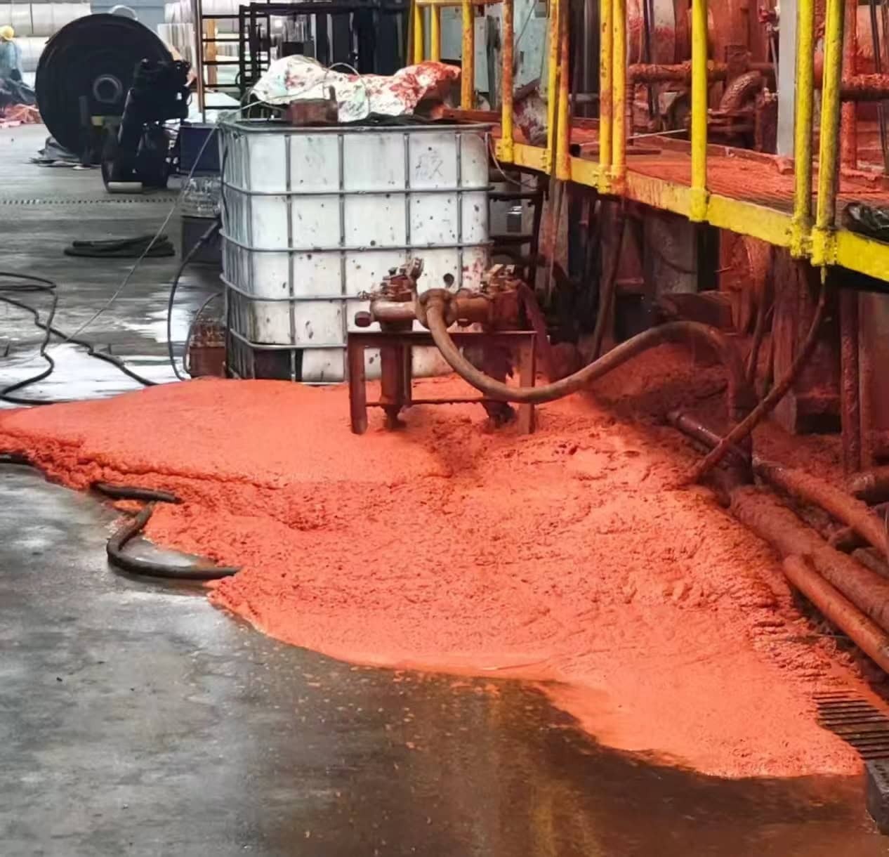 Orange-colored foam spread across an industrial floor beside hoses, pipework and an IBC container